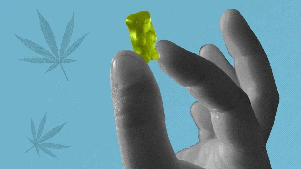 A hand holding a green THC gummy bear with cannabis leaves in the background, highlighting the edible form of cannabis for wellness benefits.